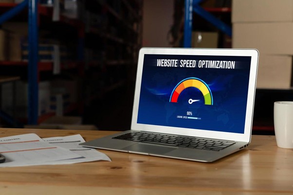 : A laptop on a wooden desk showing a website speed optimization gauge at 90% performance.