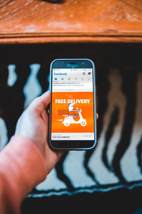 A person holding up a smartphone displaying a Facebook ad 